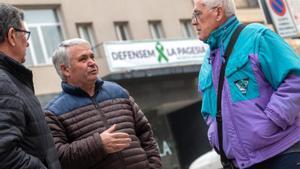 El concejal de Agricultura de Alcarràs, Agustí Camarasa (en el centro) charla con dos vecinos ante la pancarta de apoyo al sector agrario colgada en el ayuntamiento.