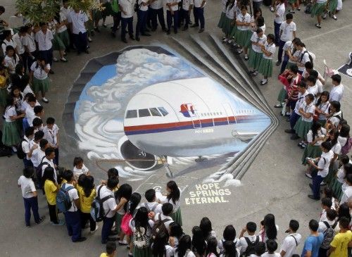 Students gather around a three dimensional artwork, based on the missing Malaysia Airlines flight MH370, that was painted on a school ground in Makati city