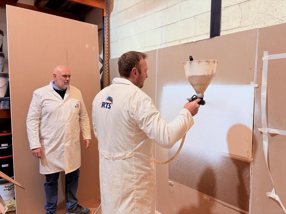 Iván Walter Checa, fundador de la empresa Revestimientos Técnicos Sostenibles, a la izquierda de la imagen en su fábrica junto a un cliente que practica cómo aplicar una de sus pinturas