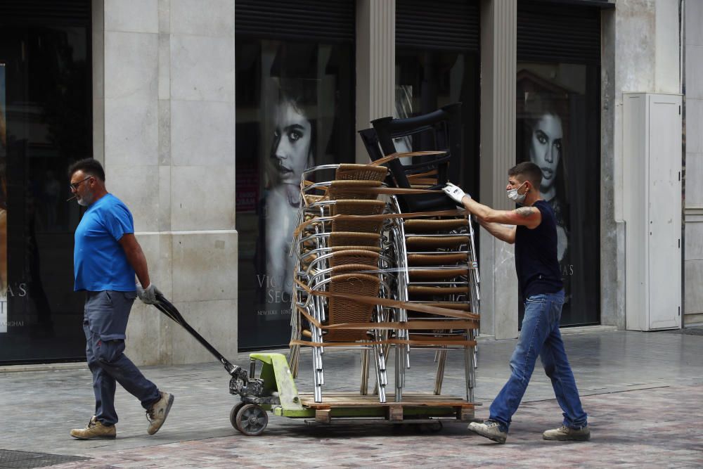 Imágenes de una lluviosa mañana de jueves en el centro de Málaga, donde al paisaje ya habitual de pocas personas y la mayoría de ellas con guantes y mascarillas se le han añadido los preparativos de bares, cafeterías y terrazas que se preparan para el inminente cambio de fase de la desescalada de la ciudad.