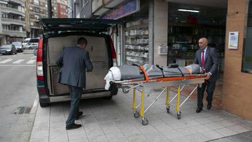 Empleados de la funeraria meten el cadáver en un furgón mortuorio.