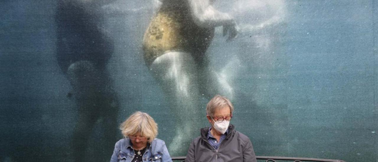 Dos personas descansan en la plaza del Mercado Central de Alicante ante una de las intervenciones fotográficas de PhotoAlicante