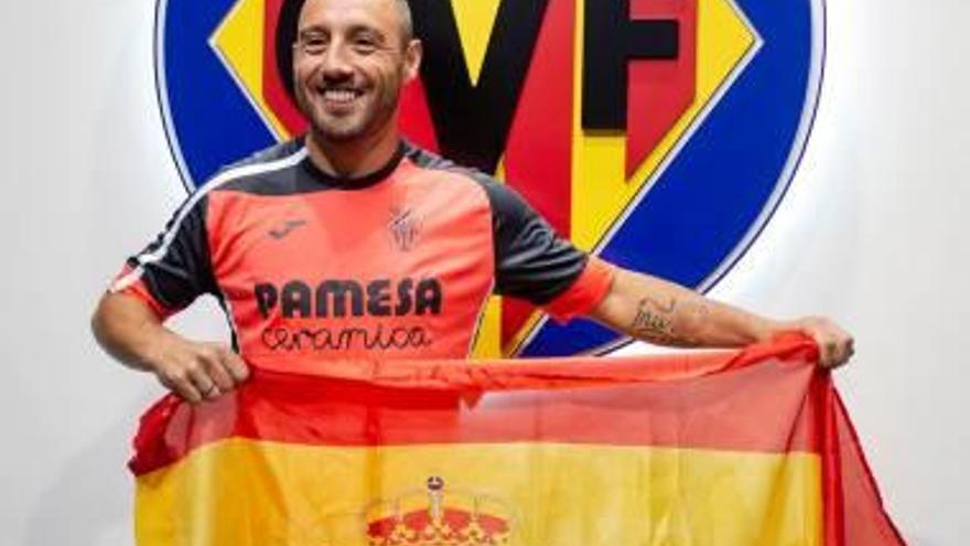 Cazorla posa sonriente con la bandera de España frente a un escudo del Villarreal en la Ciudad Deportiva.