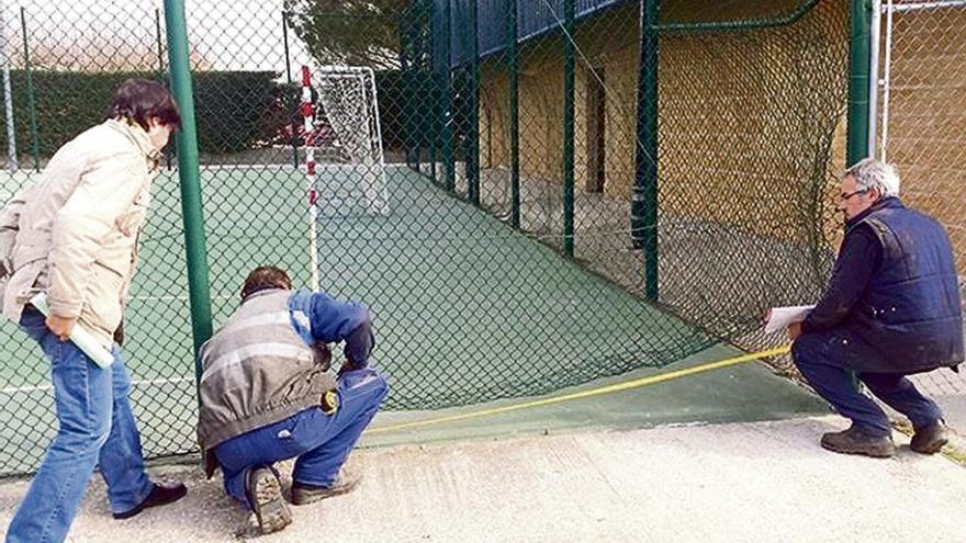 Los operarios arreglan una malla de la pista de fútbol en la instalación deportiva.