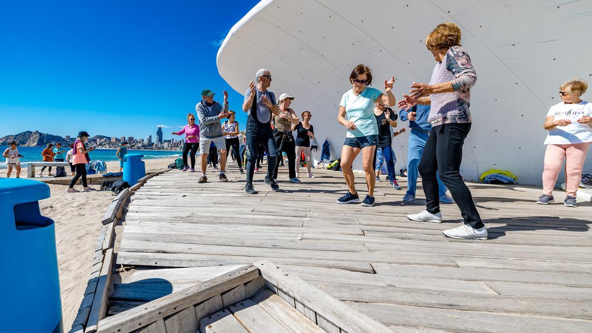 Jubilados bailando en una pasarela de madera en la Playa de Poniente de Benidorm.