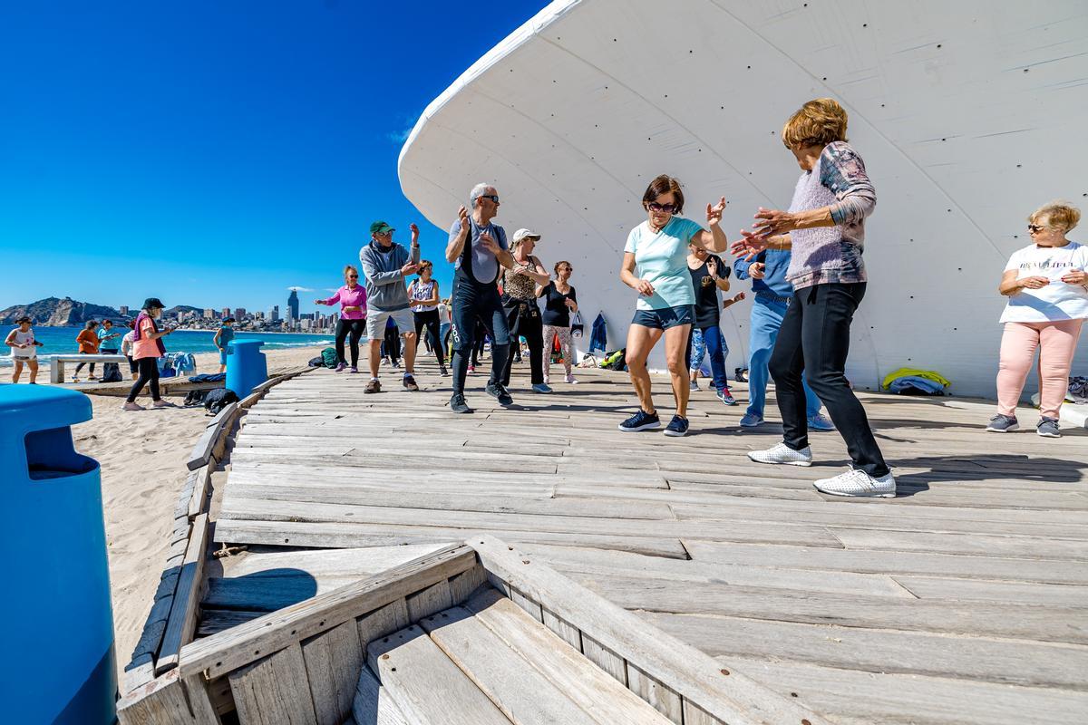 Jubilados bailando en una pasarela de madera en la Playa de Poniente de Benidorm.