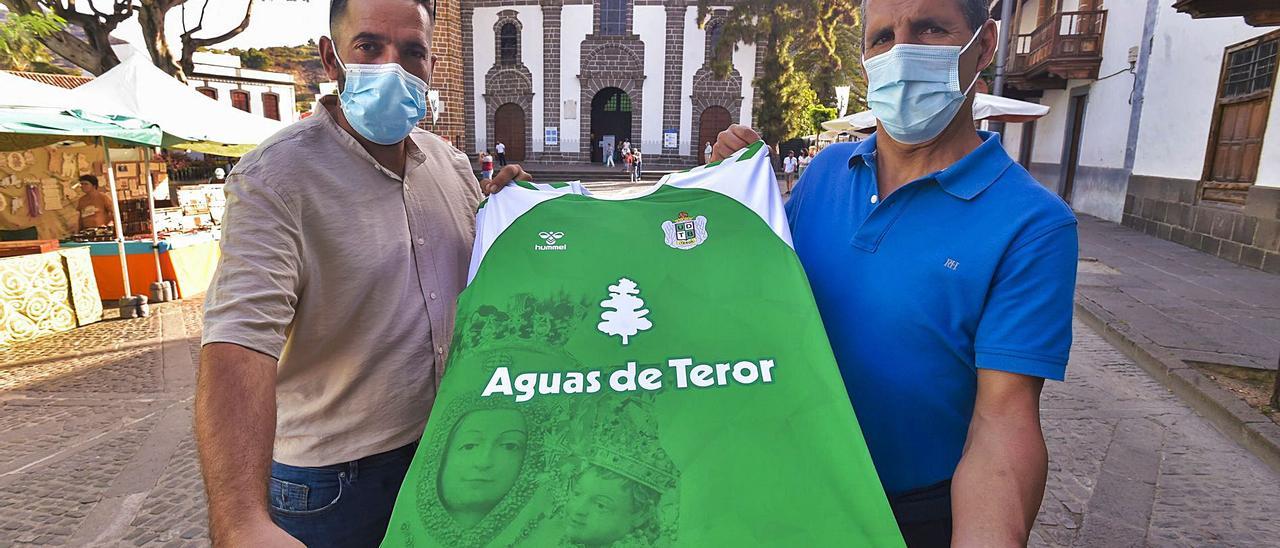 Manolo González –izquierda–, presidente de la UD Teror, y Marcos Moreira, entrenador de porteros, con la nueva camiseta del equipo delante de la basílica, ayer. | | ANDRÉS CRUZ