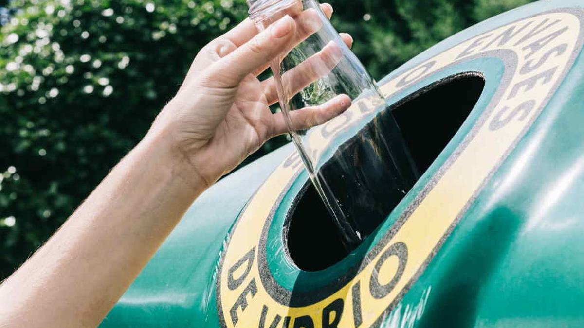 Una persona tirando un envase de vidrio a un contenedor verde