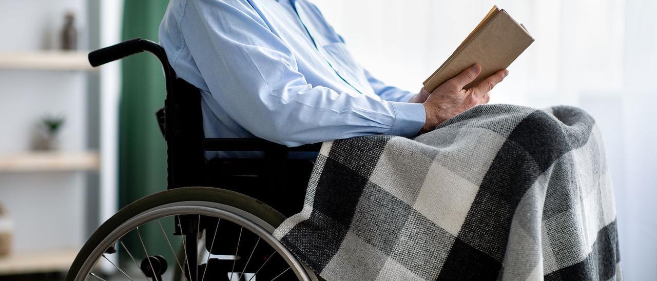 Una persona mayor, en silla de ruedas, leyendo un libro