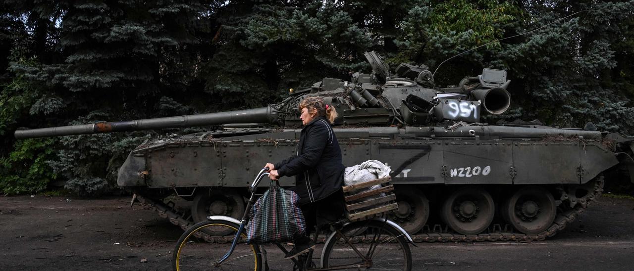 Una mujer en bicicleta junto a un tanque. EPC