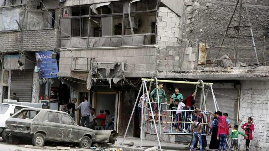 Unos niños juegan en un columpio colectivo junto a edificios bombardeados en Alepo. // Reuters