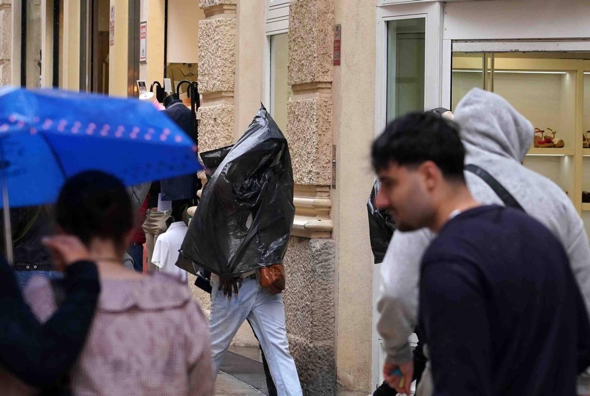 Varias personas se refugian del la lluvias con paraguas y chubasqueros