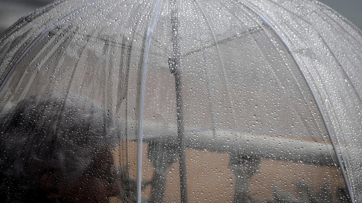 Una mujer se cubre de la lluvia bajo un paraguas.