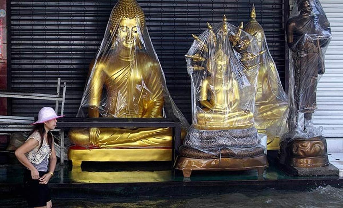 Una dona passa davant d’una botiga que ven estàtues de Buda, en una zona inundada de Bangkok.