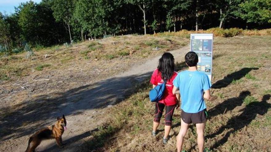 Dos personas observan uno de los paneles de la ruta, ayer, junto a los petroglifos de Poza da Lagoa. // Faro