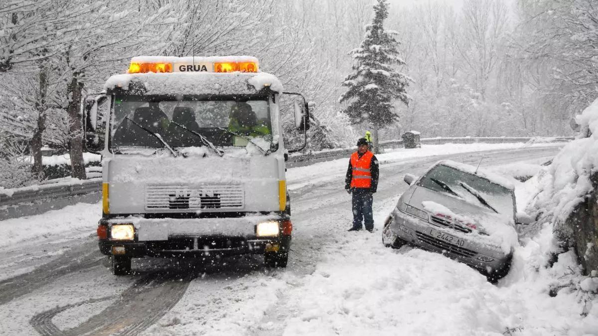 Una grúa atiende a un coche atrapado en la nieve en una carretera.