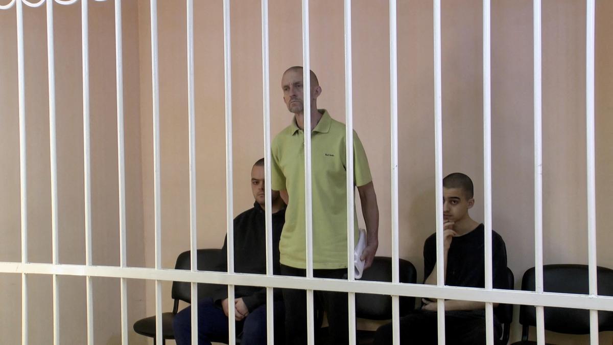 A still image shows Britons Aiden Aslin, Shaun Pinner and Moroccan Brahim Saadoun in a courtroom cage at a location given as Donetsk
