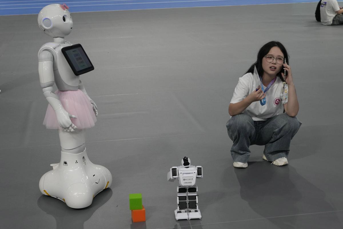 Una mujer descansa cerca de robots de diferentes tamaños en los Juegos Mundiales de Robots Humanoides celebrados en Pekín, China, el viernes 15 de agosto de 2025. (AP Photo/Ng Han Guan)