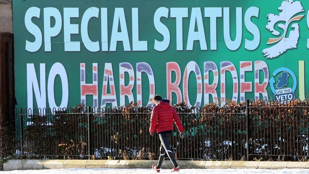 Un peatón pasa junto a un cartel en Belfast sobre el Sinn Féin rechazando una frontera dura.