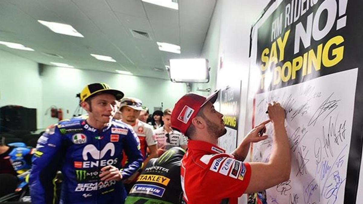 Andrea Dovizioso firma, en Doha (Catar), en un papel donde se pide limpieza en su deporte, mientras Valentino Rossi guarda turno.