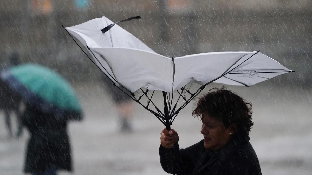 Una mujer sujeta un paraguas roto en Santiago