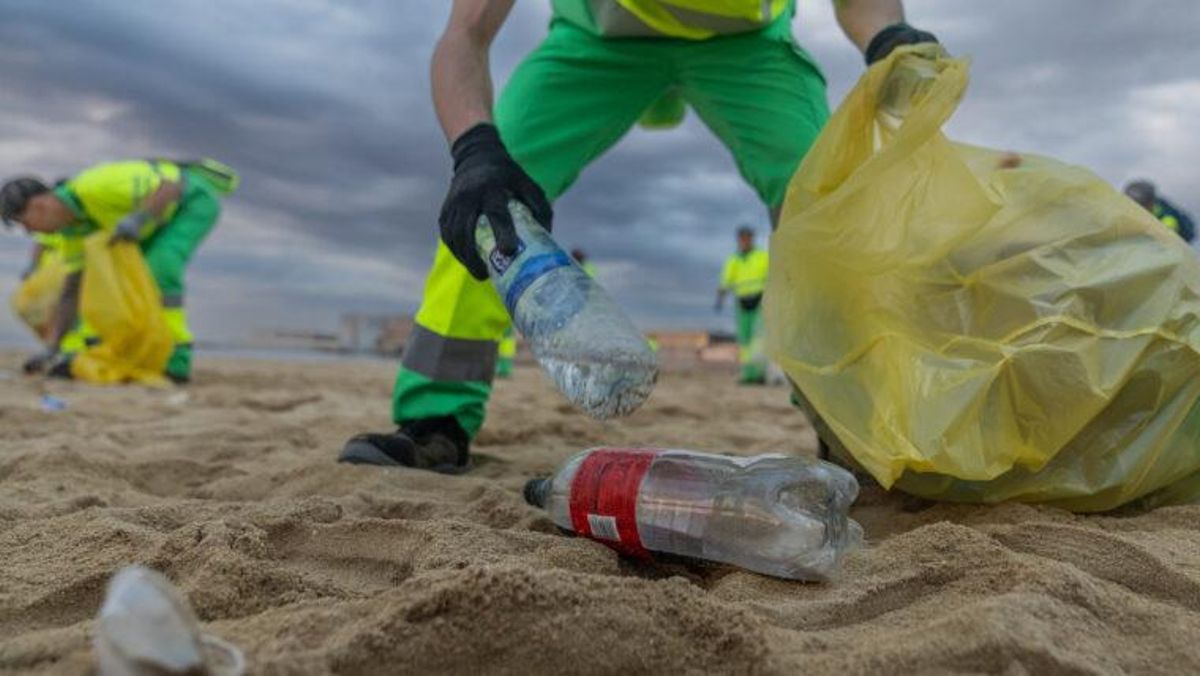 Un trabajador de la limpieza recoge botellas de plástico en la playa