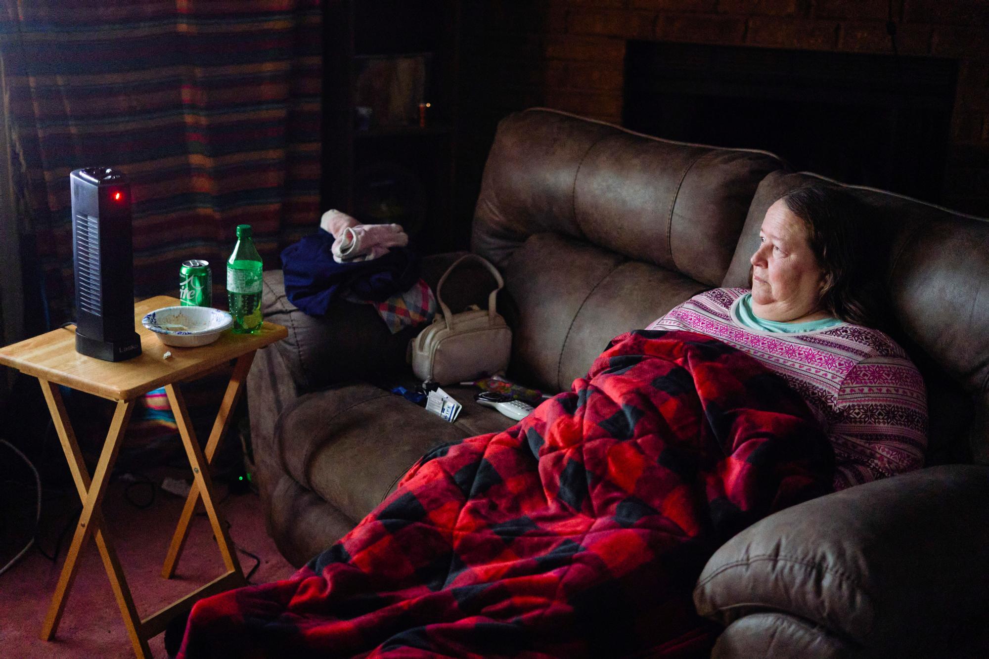 Una mujer se protege del frío con una manta y una pequeña estufa en su casa de Fort Worth.