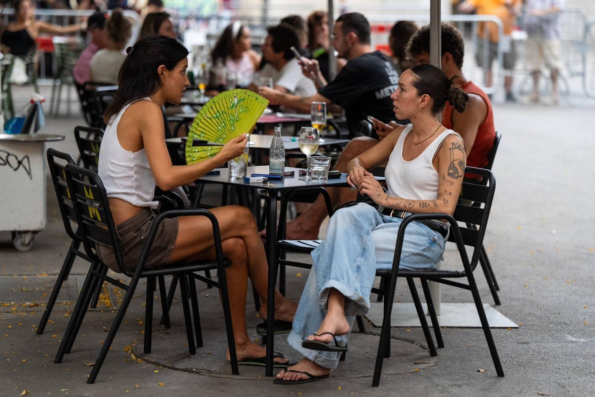 Gente sentada en un bar y abanicándose para hacer frente a las altas temperaturas en Barcelona.