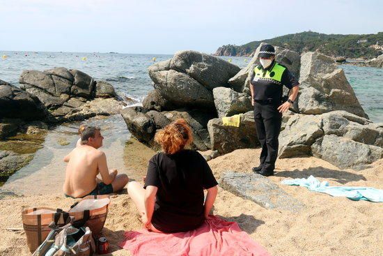 Una agent cívic a la platja del Canadell de Calella informant uns banyistes de les mesures de seguretat