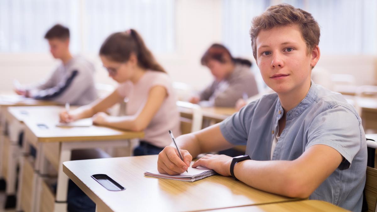 Adolescente sentado en el escritorio en el aula llena de alumnos durante la lección.