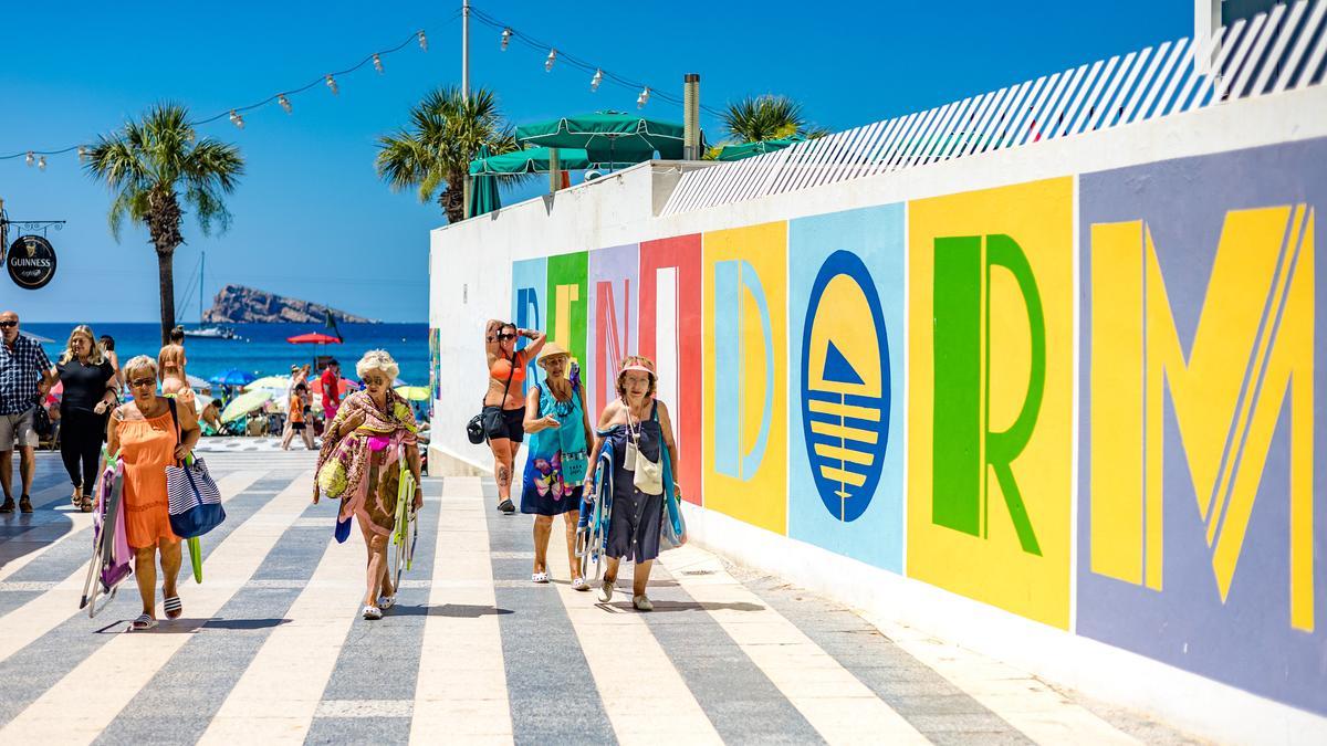 Un grupo de mujeres frente a un cartel de Benidorm junto a la playa de Levante.