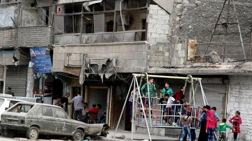 Unos niños juegan en un columpio colectivo junto a edificios dañados por bombardeos en un barrio de Alepo.