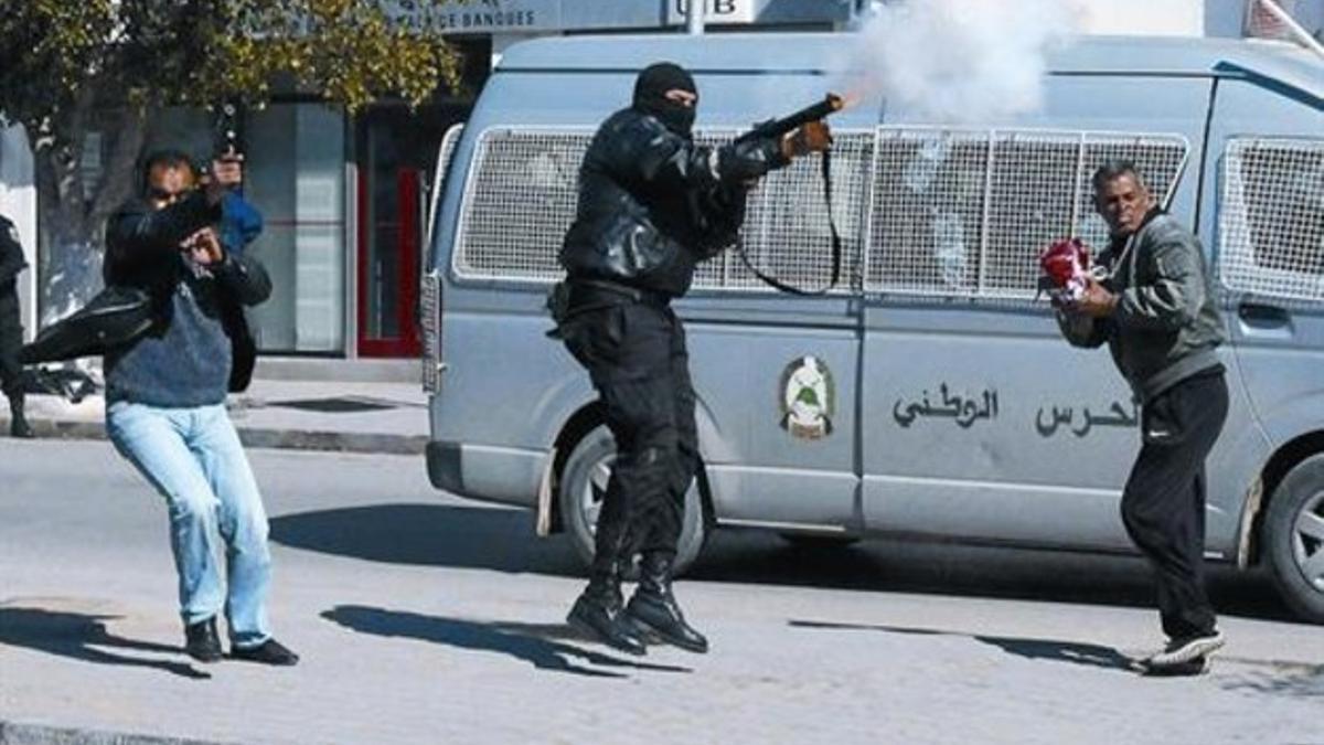 Un policía lanza gases lacrimógenos y otro dispara al aire durante una manifestación en la localidad de Gafsa.