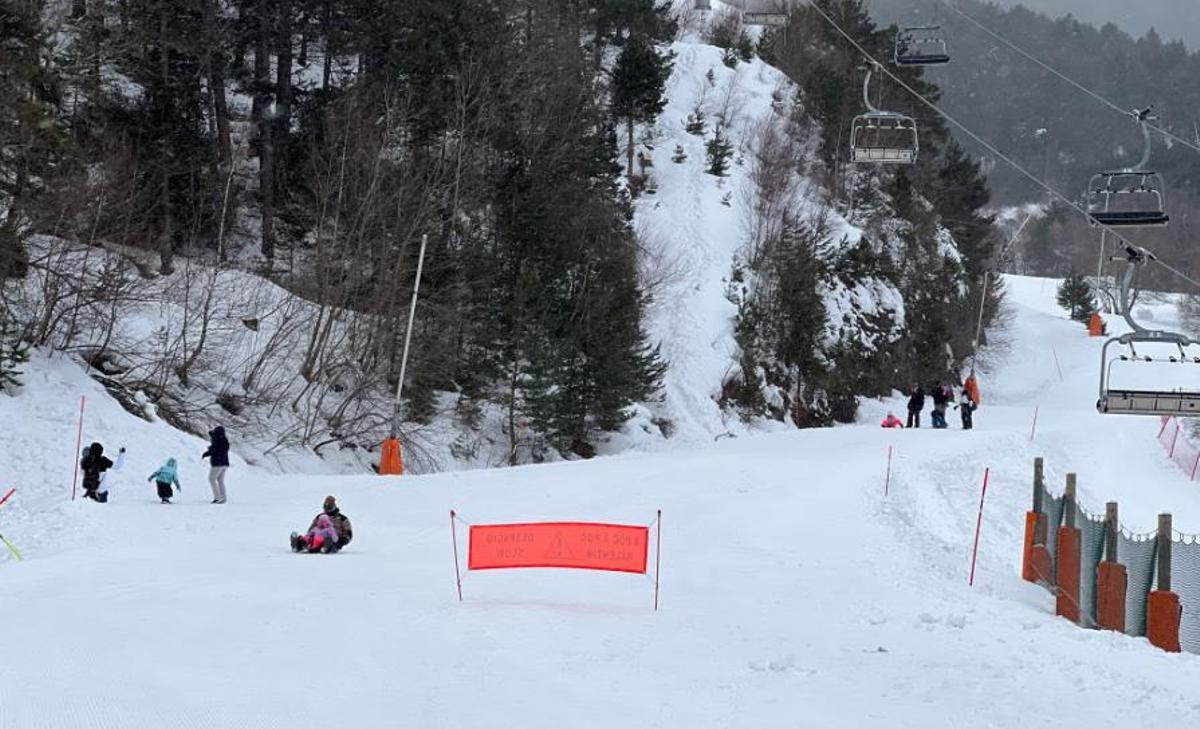 Diverses famílies gaudint de la neu a la base de l’estació d’Espot, que ha tancat pel vent i on es veu un telecadira buit i aturat