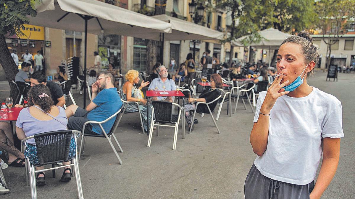 Una mujer se fuma un cigarrillo alejada de la terraza de una cafetería, en Barcelona.   | // JORDI COTRINA