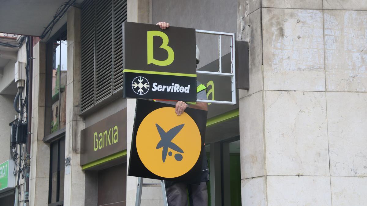 Un operario cambia el logotipo de Bankia por el de CaixaBank en una oficina.