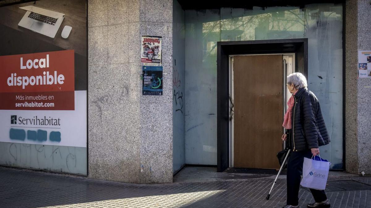Una mujer pasa, ayer, ante la puerta blindada de la antigua sucursal bancaria de Sant Ferran. | B.RAMON
