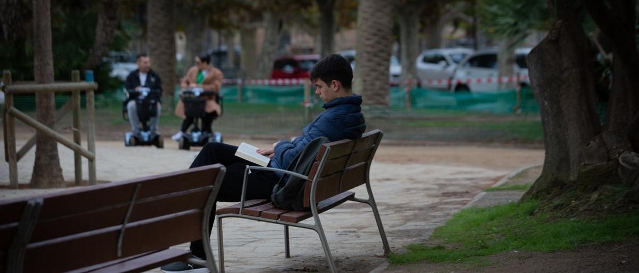 Un joven lee un libro en un parque.