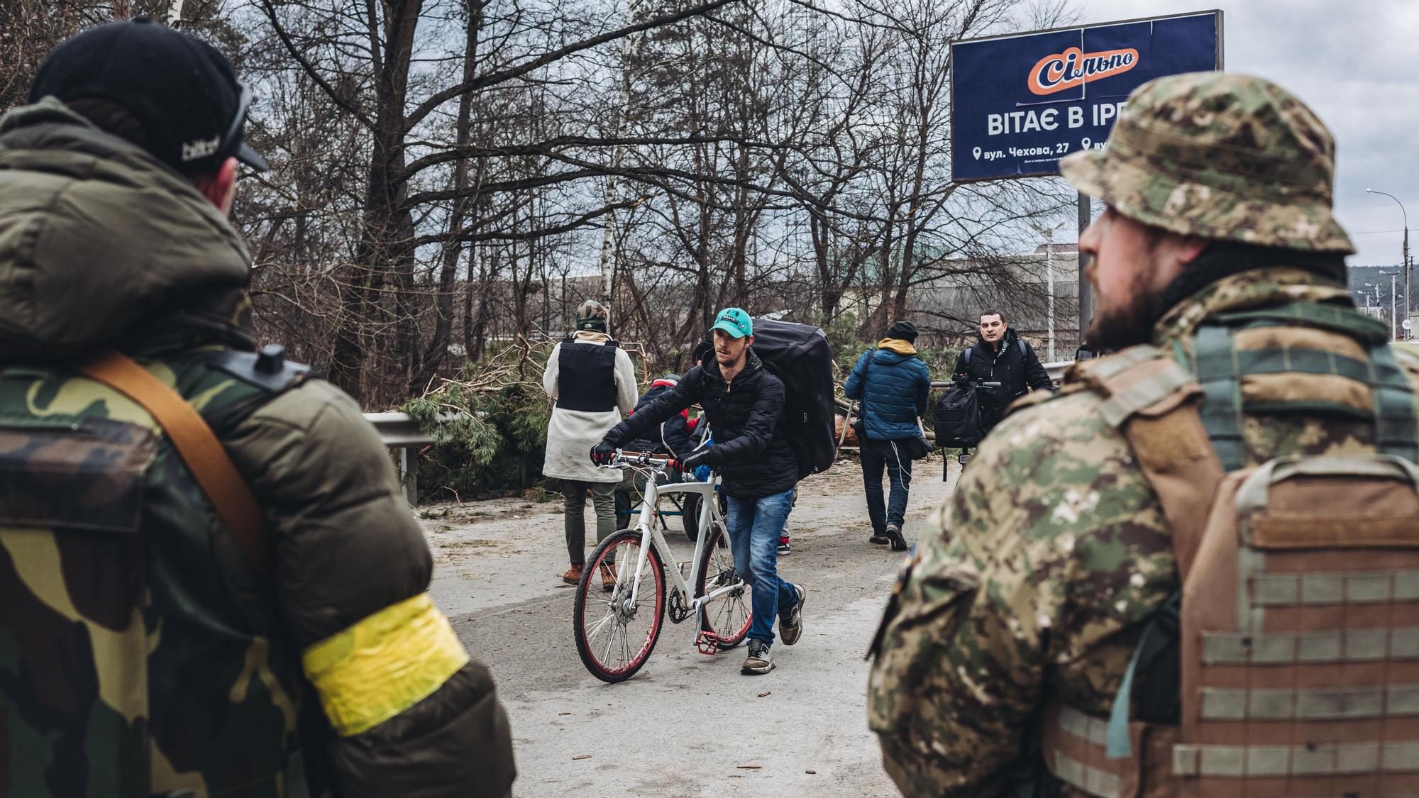 Un joven camina, junto a su bici, mientras dos soldados ucranianos le observan en Irpin (Ucrania).