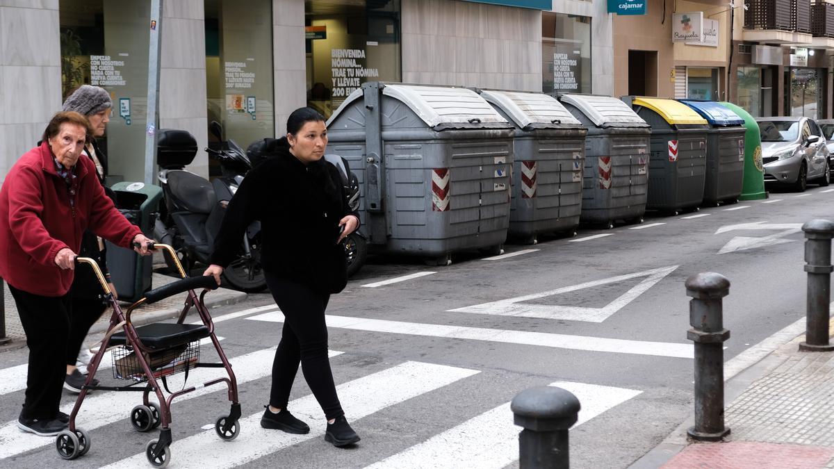Varias mujeres caminan en una calle céntrica junto a una hilera de contenedores.