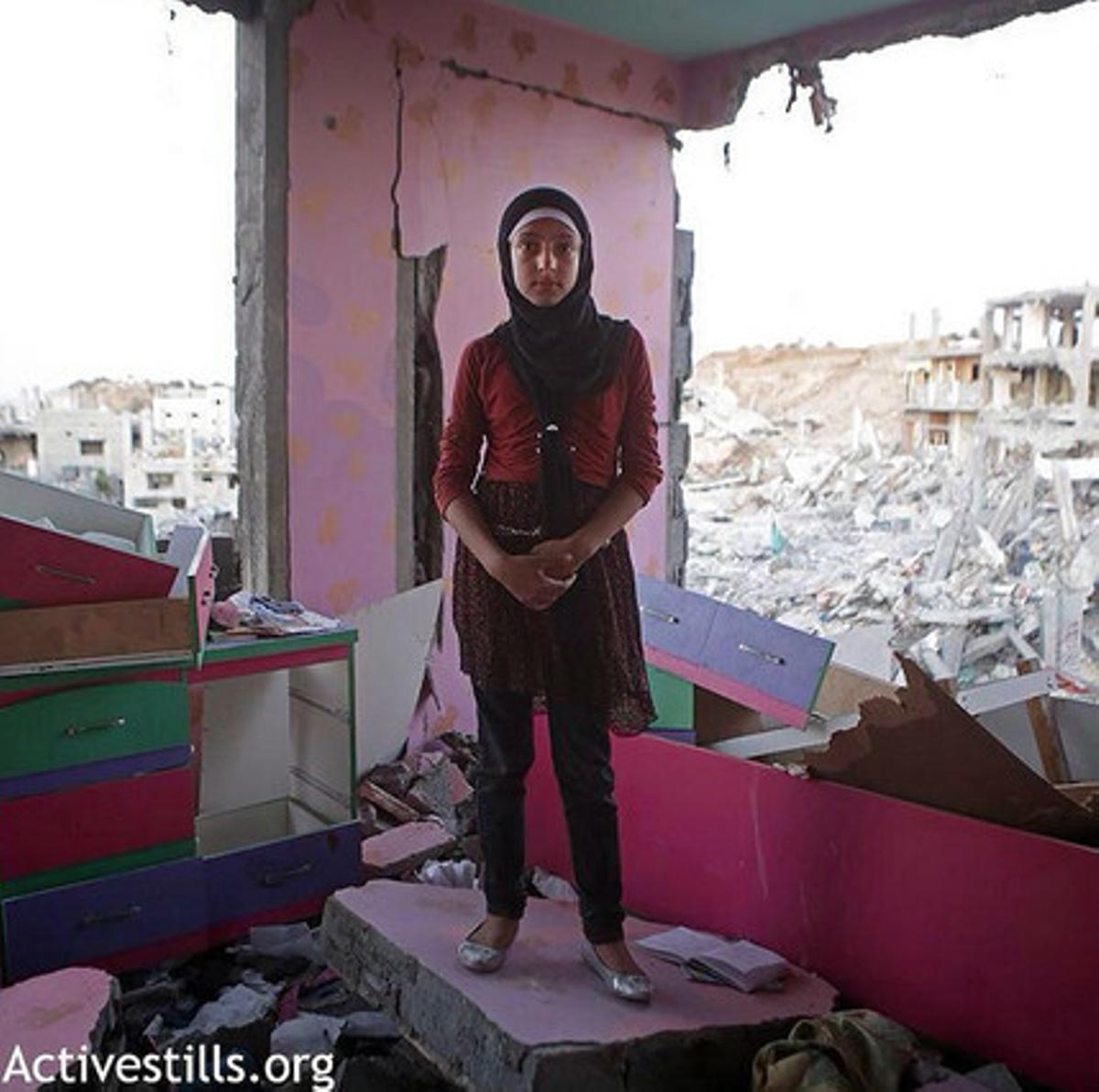 Una noia, a la seva habitació, amb les parets destruïdes pels bombardejos.