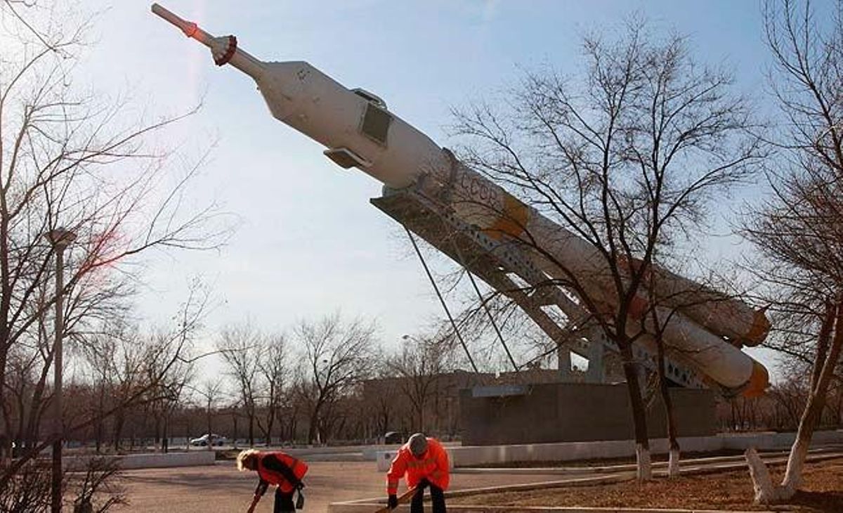 Treballadors municipals netegen el carrer davant d’un coet Soiuz instal·lat com a monument al Kazakhstan.