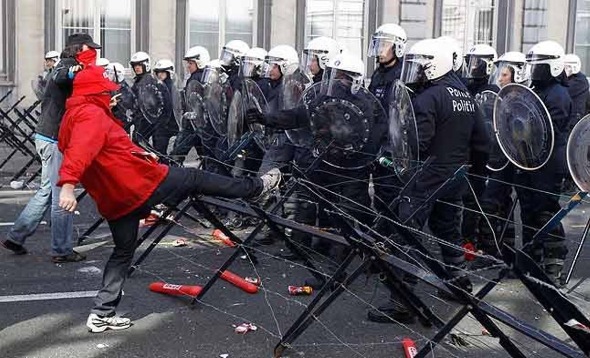 Un manifestant dóna puntades de peu a una barrera antiavalots durant una protesta de treballadors per demanar més protecció laboral en els països de la UE, a Brussel·les (Bèlgica)