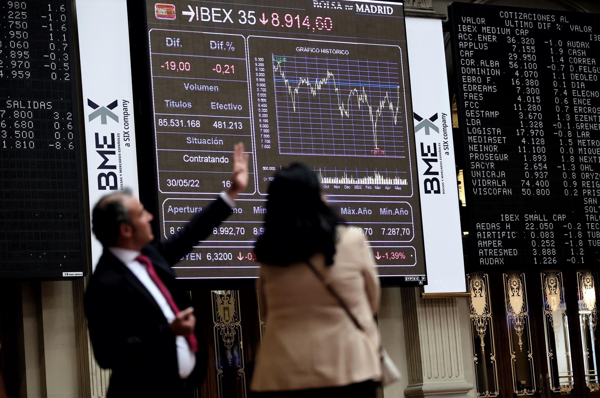 Dos personas frente a un panel de valores del Ibex 25 en el Palacio de la Bolsa