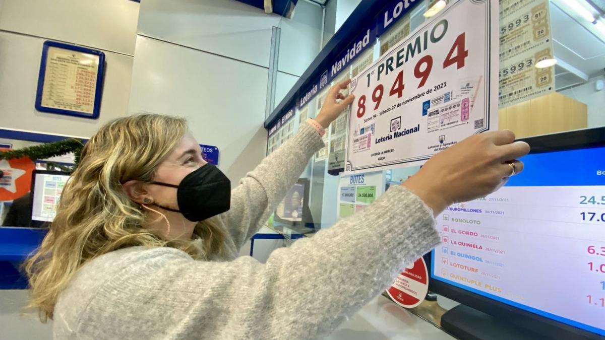 Laura Córdoba pega uno de los carteles del premio de Lotería Nacional en su administración de La Merced.