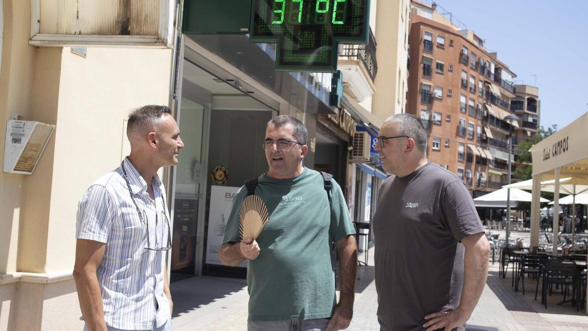 Tres hombres conversando sobre el calor bajo un termómetro al sol en Xàtiva que a media mañana ya marcaba 37 ºC.