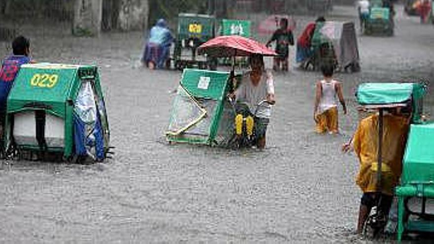 Motociclistas filipinos cruzan una calle inundada por torrenciales lluvias en San Juan, este de Manila, Filipinas.