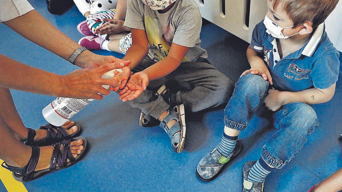 Una mujer echa gel desinfectante en las manos a un niño en un centro educativo. |   // JESÚS DIGES