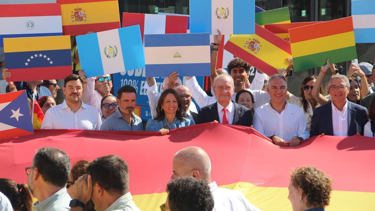 Los dirigentes del PP de Málaga despliegan una bandera de España junto a extranjeros hispanohablantes que residen en Málaga.