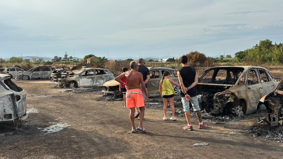 Varias personas miran algunos de los coches calcinados en Peñíscola, este sábado, tres días después del incendio.